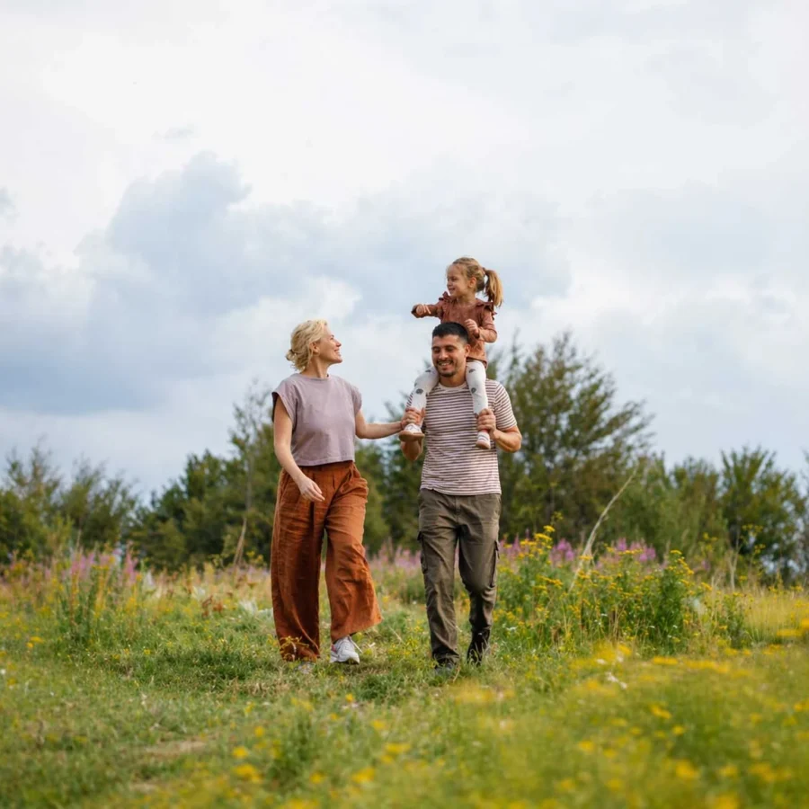 Ouders wandelen door een bloeiend veld, hun dochter op de schouders van haar vader